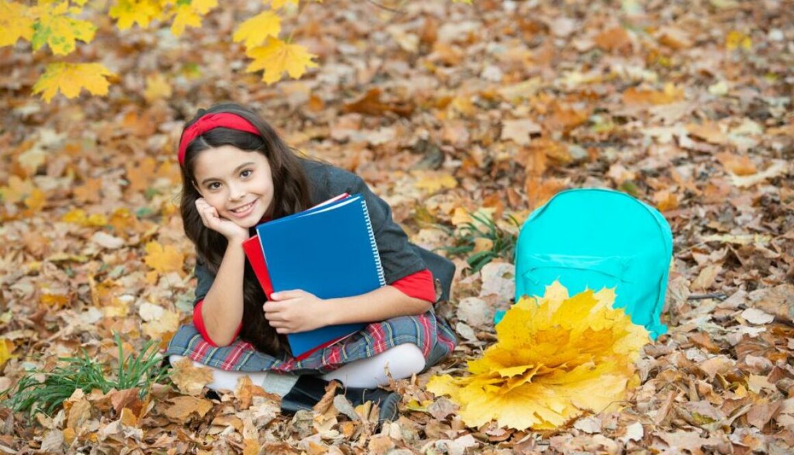 Daycare child with autumn leaves and books