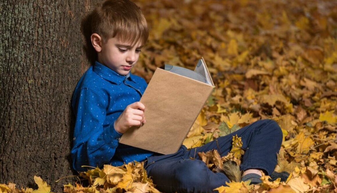 Daycare boy sits on fallen leaves