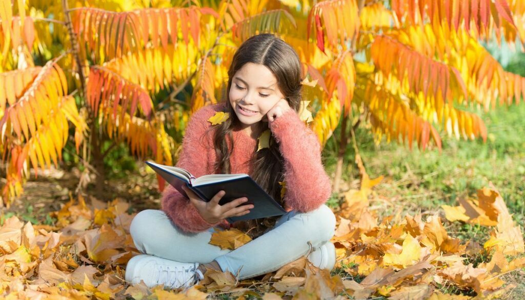 Daycare child reading book in an autumn day